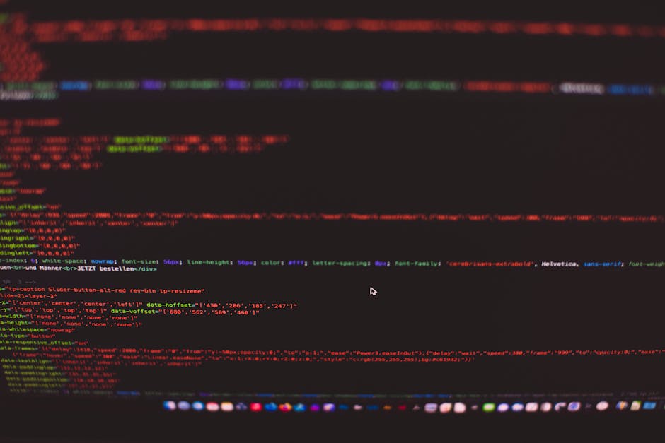 A close-up photograph of a computer screen displaying colorful lines of code with red, green, blue, and purple syntax highlighting on a black background. The screen shows HTML and CSS elements, includ